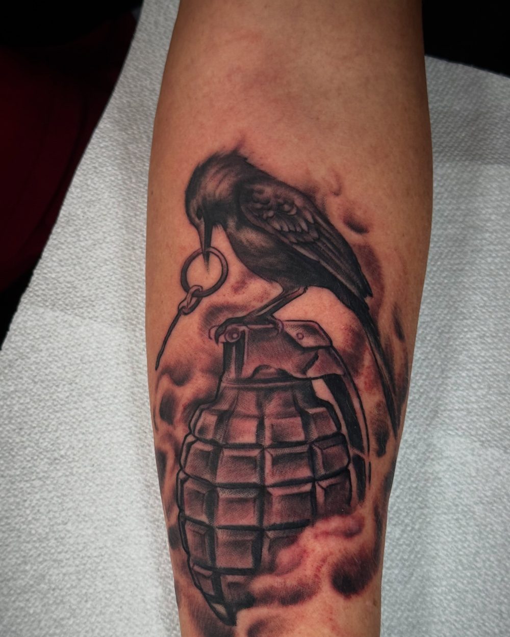 A fresh black and grey crow and grenade tattoo just after the session