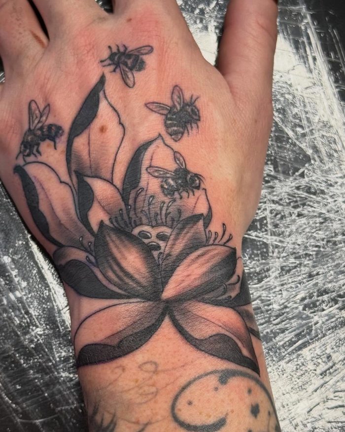 A fresh black and grey lotus and bees tattoo on a hand