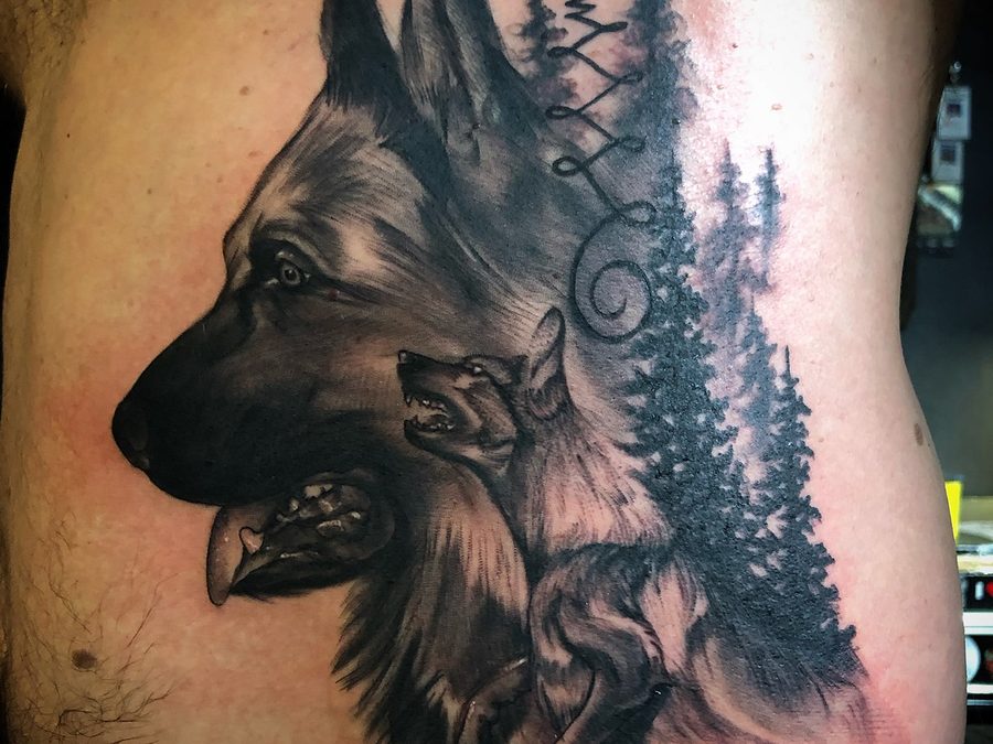 German shepherd and pines tattoo in black and grey by Jeremy Sramek